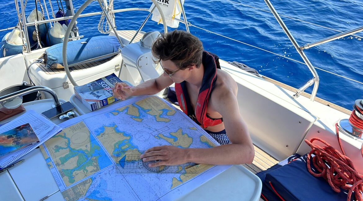 rya day skipper course A realistic image of a person working on charts on a sailboat.